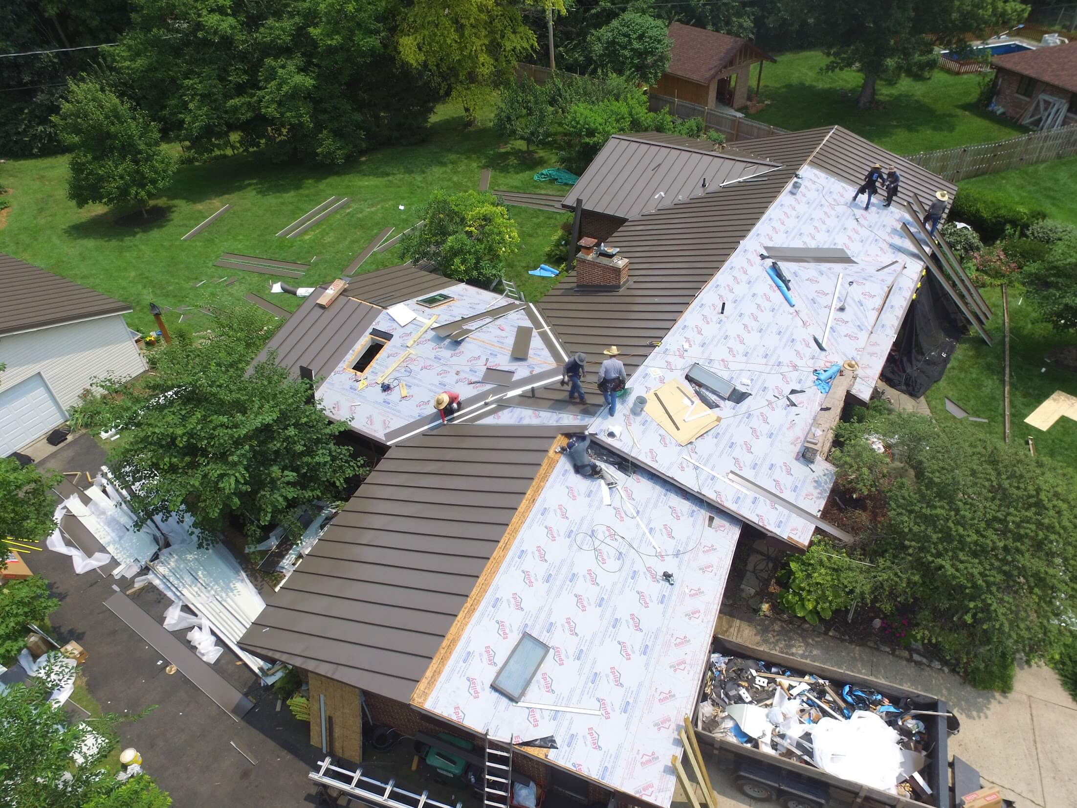 Aerial view of a house roof under construction with workers installing metal roofing panels and scattered tools.