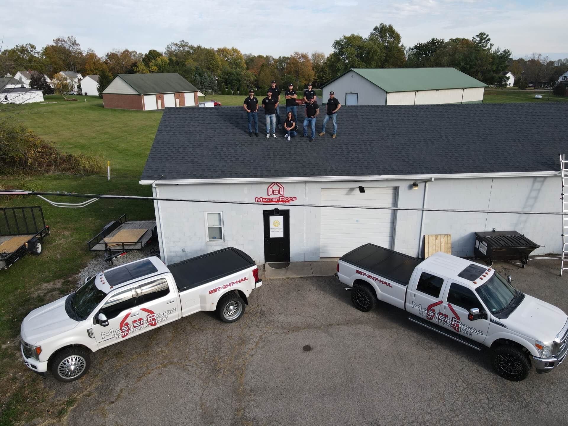 Group of workers in black shirts stand on a roof above a service building with MasterRoof signage visible on the wall beneath them.
