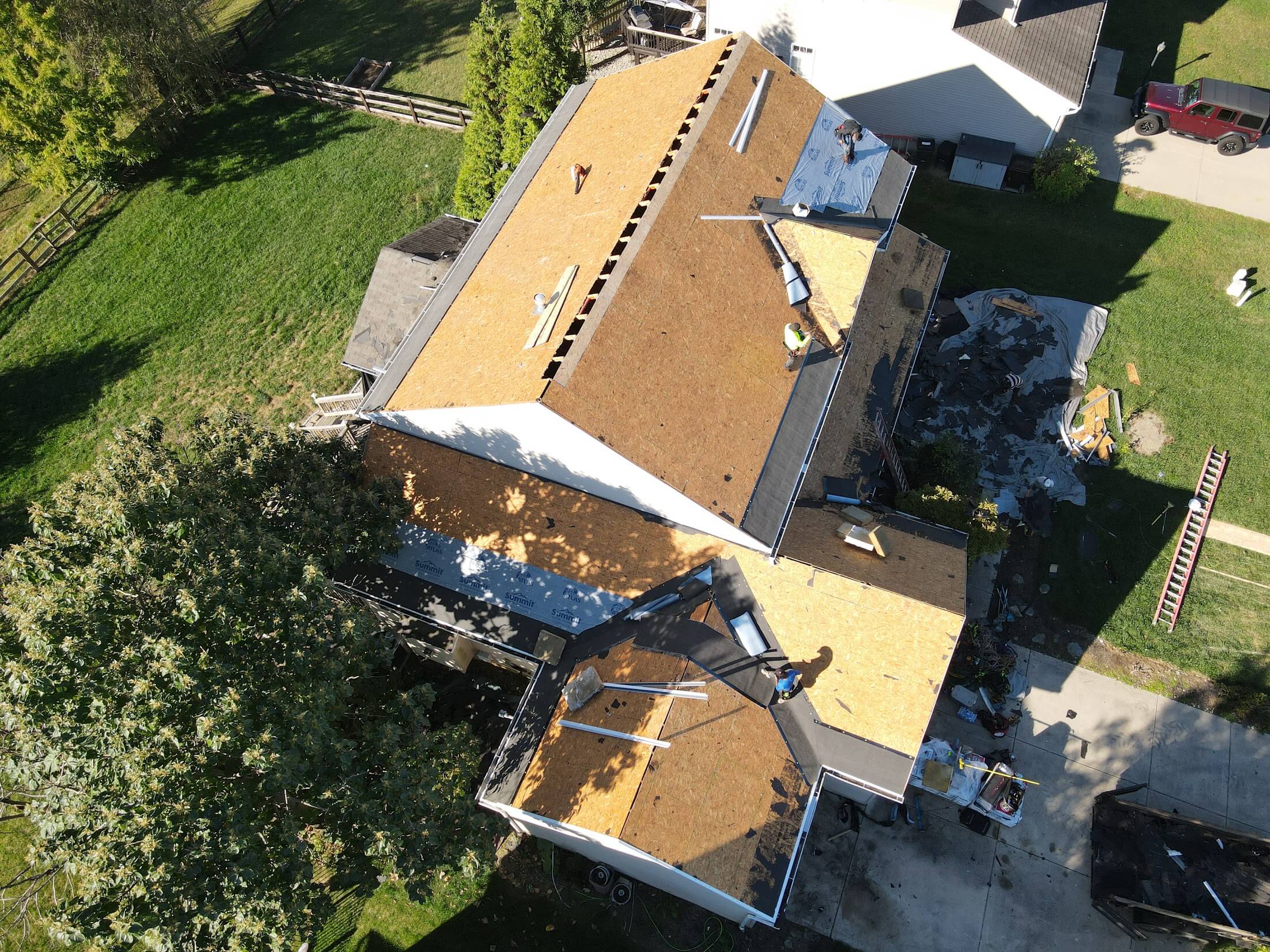 Aerial view of a two-story house under construction; plywood roof sheathing and workers on the roof seen from above.