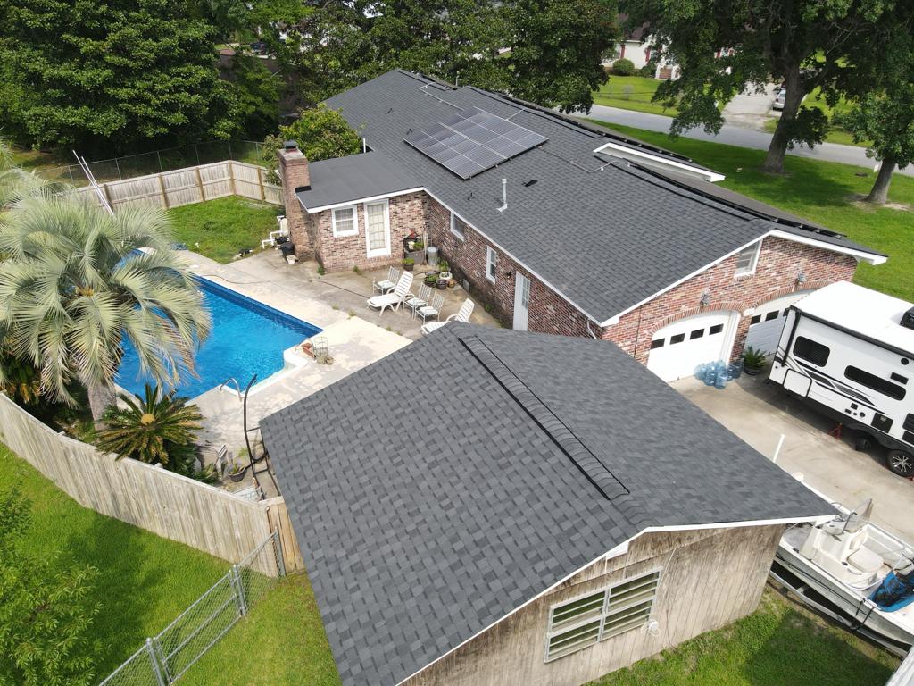Aerial view of a brick house with a gray roof and solar panels, a blue rectangular pool, patio chairs, and an RV in the driveway.